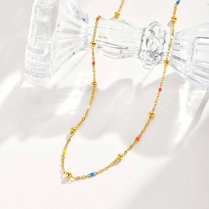 Detail of gold beaded necklace with colorful enamel charms on a glass holder