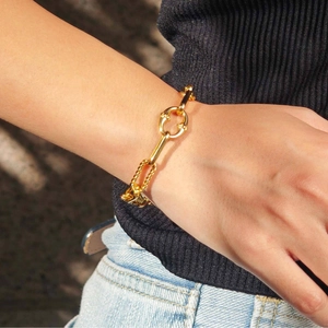 Dettaglio di un bracciale a catena dorata indossato sopra una manica in maglia nera chic