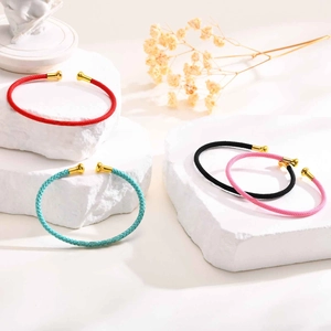 Detailed view of colorful woven cord bangles with gold metal ends on stone podium