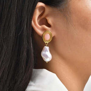 Detail of gold drop earring with pink gemstone and baroque pearl worn by a model