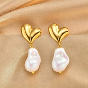 Detailed shot of golden heart earrings with purple baroque pearl on champagne silk fabric