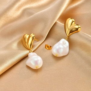 Close-up of golden heart earrings with baroque pearls on elegant gold silk fabric