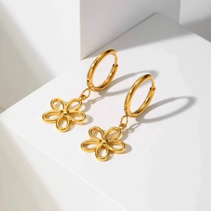 Gros plan de boucles d'oreilles fleurs dorées polies sur fond géométrique blanc épuré