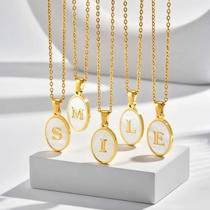 Detail of oval gold pendant with white shell inlay and engraved letters on a stone stand