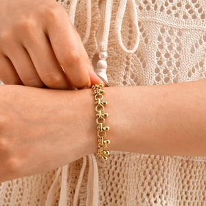 Close-up of golden link bracelet with teardrop charms worn against a knitted background