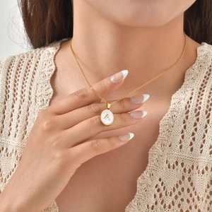 Close-up of golden letter A necklace with white shell pendant on a model in knit top
