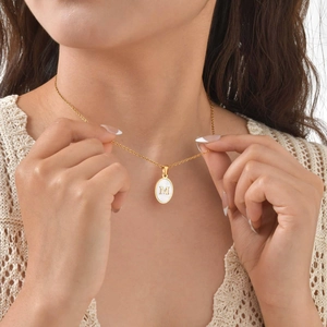 Detail of gold oval pendant with white shell inlay and letter M on a model