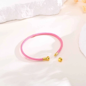 Pink woven cord bracelet with gold screw ball clasp on a minimalist stone background