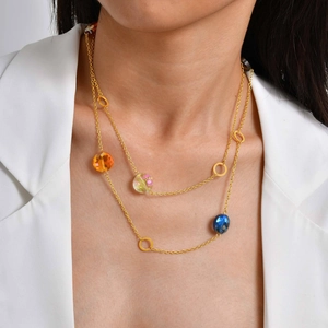 Détail d'un collier doré double épaisseur avec perles colorées sur fond de blazer blanc