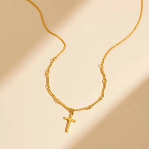 Golden stainless steel cross necklace with a unique bamboo-style link chain on beige background