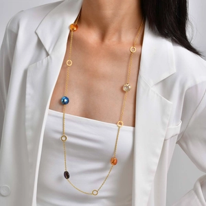 Détail d'un long collier en or avec des perles colorées porté sur un tailleur blanc