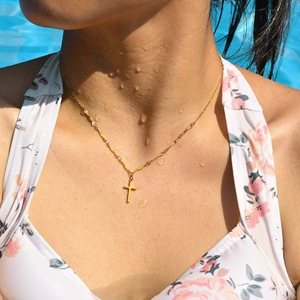 Close-up of waterproof gold cross necklace with wavy link chain on model by pool