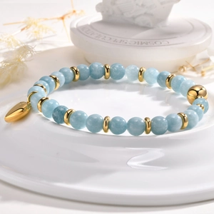 Détail d'un bracelet en perles bleu clair avec breloque cœur doré et billes polies