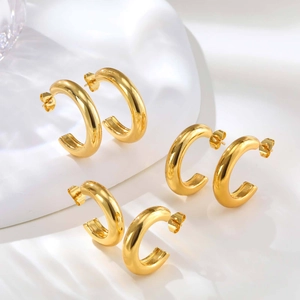 Three pairs of polished gold C-shape hoop earrings on minimalist white wave display stand