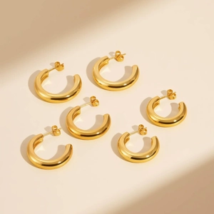 Detailed view of three pairs of golden C-shaped hoop earrings in various sizes on beige steps