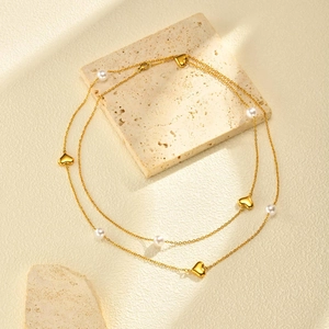 Détail du collier doré multicouche avec cœurs et perles sur fond de pierre neutre