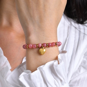 Gros plan d'un bracelet en perles roses avec pendentif cœur doré au poignet d'une femme