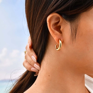 Elegant gold C-shaped stainless steel hoop earrings worn by a model in outdoor light