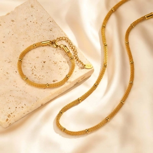 Elegant gold-plated mesh chain jewelry set with polished beads on silk background