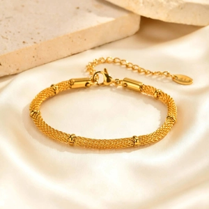 Detailed macro shot of the golden mesh tube bracelet on a soft white silk background