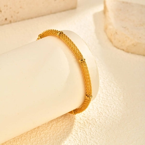 Detail of a golden mesh chain bracelet with spherical beads on a stone display