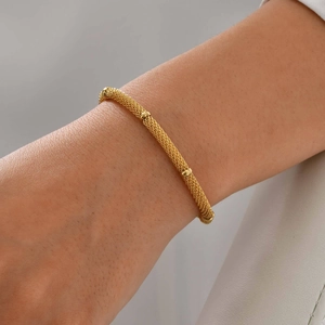 Macro detail of golden woven mesh chain bracelet with polished decorative rings on wrist