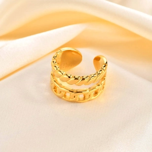 Macro di anello aperto dorato con texture a catena e corda su sfondo di raso beige chic
