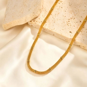 Close-up of gold mesh chain with small beads against a luxury stone and satin background
