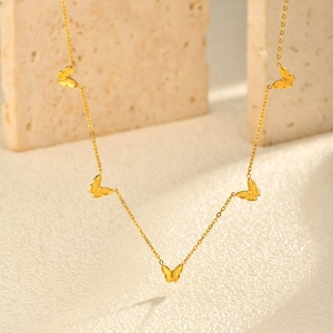 Détail d'un collier papillon doré délicat drapé sur des blocs de pierre beige épurés