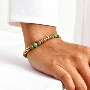 Detail of beaded bracelet with green gemstones and gold accents on woman's wrist