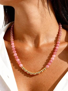 Close-up of pink crystal and gold beaded necklace worn on neck with warm sunlight