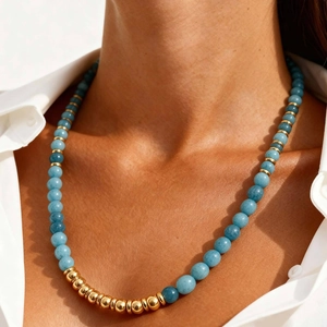 Blue beaded necklace with gold metal accents worn by a model in a white shirt