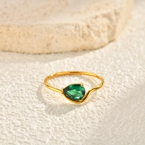 Macro detail of a golden ring featuring a green pear-cut zircon and delicate metal band
