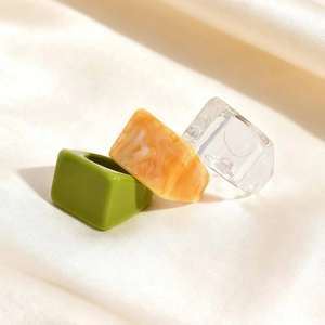 Close-up of three thick resin square rings in green, amber, and clear on satin fabric