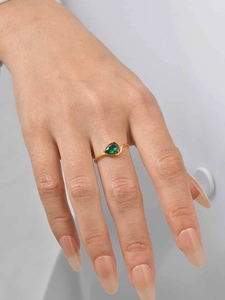 Detail shot of pear-cut green gemstone ring with gold S-shaped band on finger
