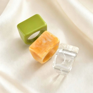 Three minimalist thick resin square rings in green, amber, and clear on silk background