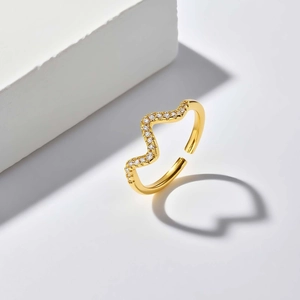 Golden wave ring casting a heart-shaped shadow on a minimalist white surface