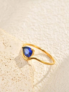 Macro detail of wave-shaped golden ring featuring a pear-cut blue zircon on stone base