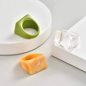 Minimalist resin rings set featuring green, transparent, and marble orange designs on a pedestal
