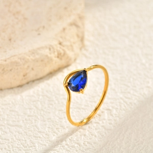 Detailed close-up of golden teardrop blue zircon ring with wavy band design