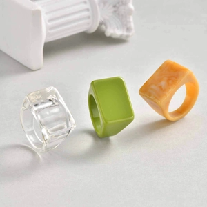 Three chunky geometric resin rings in clear, green, and amber marble on a minimalist base