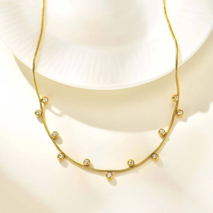 Golden snake chain necklace with round white cubic zirconia charms on white ceramic plate