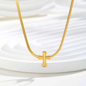 Detail eines goldenen Kreuzanhängers an einer Schlangenkette auf weißem Dekor