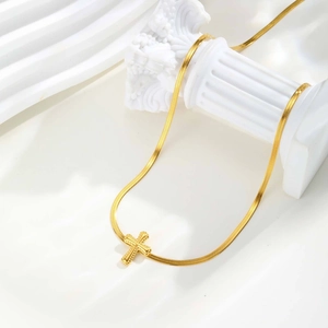 Nahaufnahme des goldenen Kreuzanhängers mit Perlenrand an einer glatten Schlangenkette