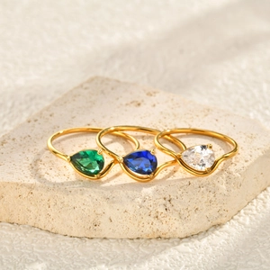 Gold plated wave rings featuring colorful pear cut cubic zirconia on a stone surface
