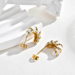 Vue détaillée de boucles d'oreilles en C dorées avec émail blanc sur décor en pierre