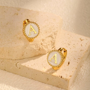 Close-up of gold huggie earrings with white enamel disc and letter A detail on stone