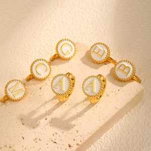 Golden stainless steel hoop earrings with white enamel initial pendants on stone background