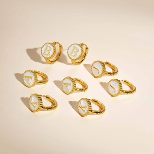 Close-up of gold round initial earrings with white inlay and beaded edge detail