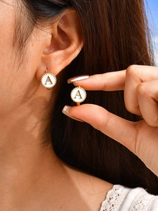 Detail of a gold letter A earring with white enamel and a beaded metal frame on ear